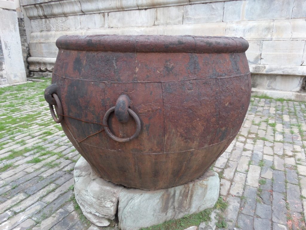 Large historic fire water cauldron beside a Forbidden City hall wall