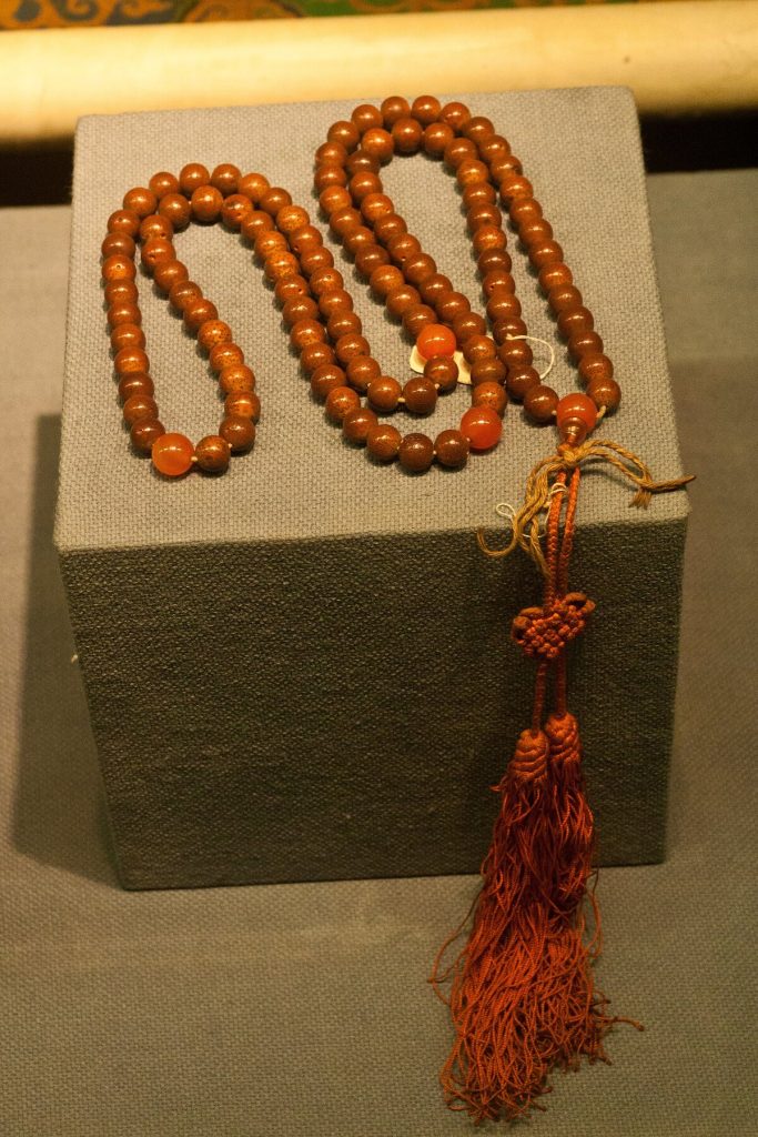 Orange Buddhist prayer beads displayed in a museum case at the Capital Museum