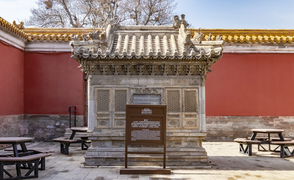 A small historic stone structure against the red wall at Beijing Imperial Ancestral Temple